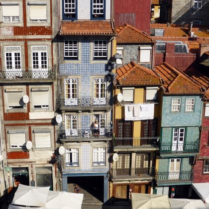 Multi-story traditional Portuguese houses in Porto with colorful facades, ornate balconies, and red clay tile roofs densely packed together.