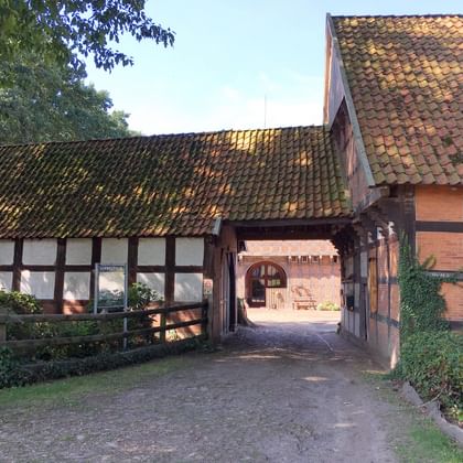 Traditional German half-timbered farm buildings with clay tile roofs surrounding a cobblestone courtyard, featuring white walls with dark wooden beams.