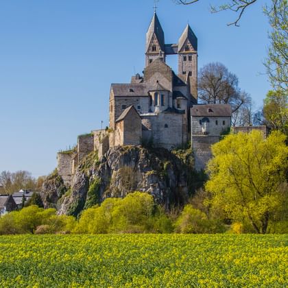 St. Lubentius Church on rocky hill in Limburg Historic St. Lubentius Church with twin towers perched on a rocky hill above a bright yellow rapeseed field in Limburg, Germany.
