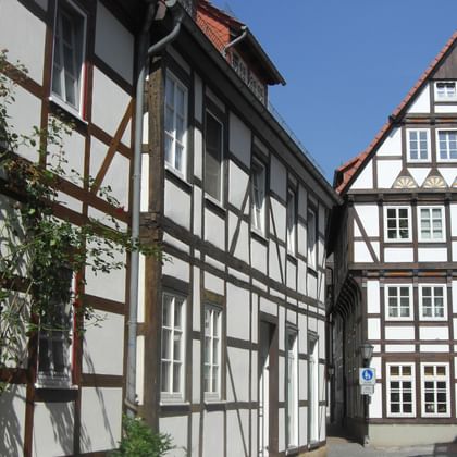 Traditional half-timbered buildings in Hameln's old town with white walls, dark wooden beams, and red tile roofs under blue sky.