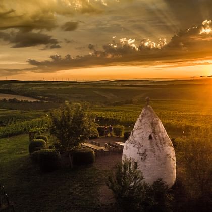 Goldener Sonnenuntergang über dem Aulheimer Tal mit weißer Steinstruktur im Vordergrund, sanften Hügeln mit Weinbergen und dramatischem Himmel.