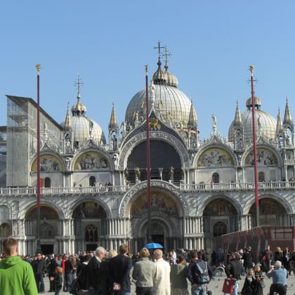 Markusdom in Venedig mit seinen charakteristischen byzantinischen Kuppeln und der verzierten Fassade. Touristenmassen versammeln sich davor.
