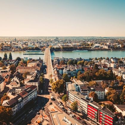 Aerial view of Kennedy Bridge spanning the Rhine River in Bonn, connecting residential areas with autumn foliage and urban buildings.