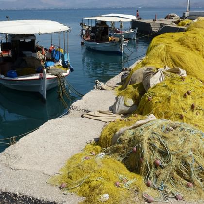 Zwei traditionelle griechische Fischerboote im Hafen von Nafplion mit großen gelben Fischernetzen auf dem Betonpier zum Trocknen.