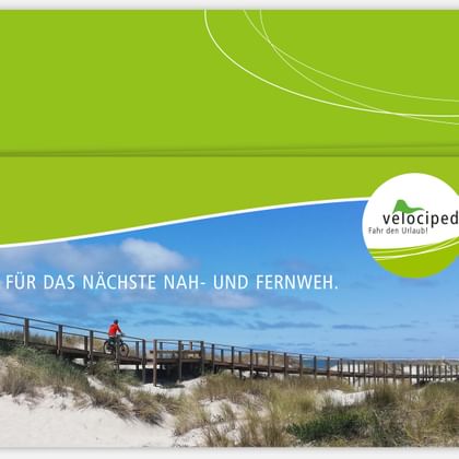 Velociped Radurlaub Geschenkgutschein Grüner Velociped Geschenkgutschein zeigt Radfahrer auf Holzsteg durch Küstendünen mit Text 'FÜR DAS NÄCHSTE NAH- UND FERNWEH'