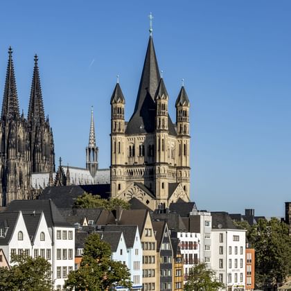 Der Kölner Dom mit gotischen Zwillingstürmen überragt die Skyline über bunten historischen Gebäuden und den Türmen von St. Martin.