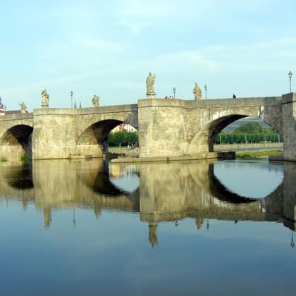 Alte Mainbrücke in Würzburg Historische Alte Mainbrücke in Würzburg mit mehreren Bögen und barocken Statuen, perfekt im ruhigen Wasser des Mains gespiegelt.