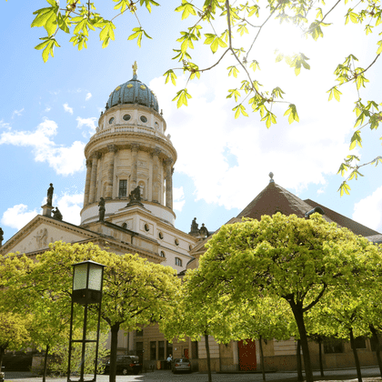 Französischer Dom am Gendarmenmarkt in Berlin mit grüner Kuppel und klassischer Architektur, umgeben von grünen Bäumen unter blauem Himmel.