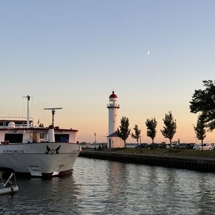 River cruise ship MS Normandie moored at harbor with white lighthouse at sunset in Hellevoetsluis, Zeeland. Crescent moon visible in sky.