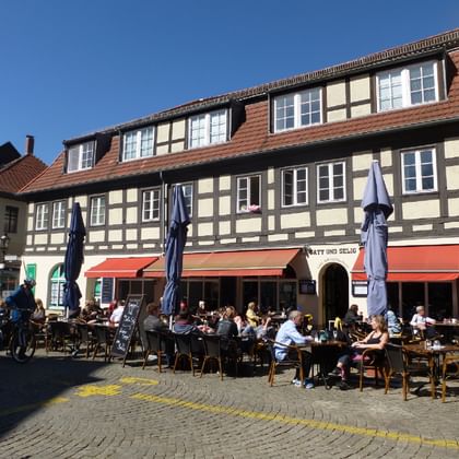Historic half-timbered building in Spandau old town with outdoor cafe seating. People dining at tables under blue umbrellas on cobblestone square.