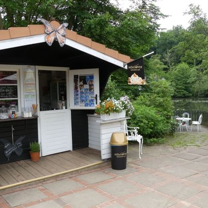 White and black kiosk with butterfly decoration on roof at waterside terrace. Flower boxes and outdoor seating visible near water in Geesthacht.