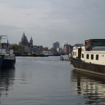 Amsterdam Grachtenblick mit historischer Kirche Blick auf Amsterdam vom Wasser aus mit Booten am Kanal und den historischen Türmen der St. Nikolaus-Basilika im Hintergrund.