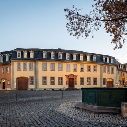 Goethes Wohnhaus am Weimarer Frauenplan Historisches gelbes Barockgebäude mit Mansarddach am Kopfsteinpflasterplatz in Weimar, Goethes ehemaliges Wohnhaus mit grüner Wasserpumpe im Vordergrund.
