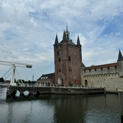Medieval gate tower with fortified walls in Zierikzee, Zeeland, connected by a white drawbridge over a canal under a cloudy sky.