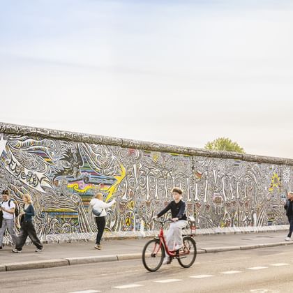 Radfahrer fährt an der bunten East Side Gallery der Berliner Mauer vorbei. Die Betonmauer zeigt kunstvolle Straßenkunst mit wirbelnden Mustern.