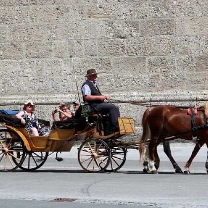 Traditionelle Pferdekutsche mit Fahrgästen in Salzburg. Zwei braune Pferde ziehen eine gelbe Holzkutsche mit Kutscher in Hut und Weste.