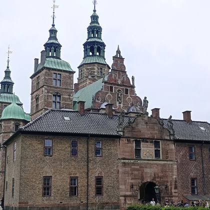 Schloss Rosenborg in Kopenhagen mit roten Backsteinmauern, Kupfertürmen und Wassergraben. Besucher spazieren um den Renaissancepalast.