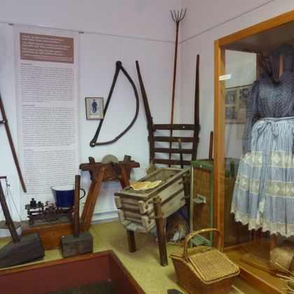 Sorbisches Museum mit traditionellen Landwirtschaftsgeräten, Holzwerkzeugen und Vitrine mit traditionellem blau-weißem Kleid.