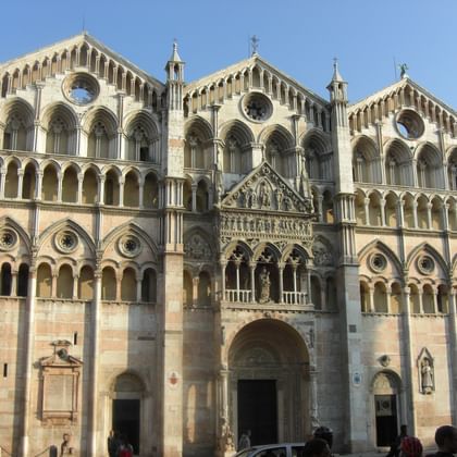 Fassade des Doms von Ferrara mit dreistöckiger romanischer Architektur, verzierten Bogengalerien, runden Rosenfenstern und geschnitzten Steindetails.