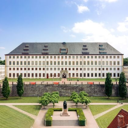 Schloss Friedenstein palace in Gotha Aerial view of Schloss Friedenstein, a large baroque palace in Gotha with symmetrical wings, formal gardens, and a monument in the courtyard.