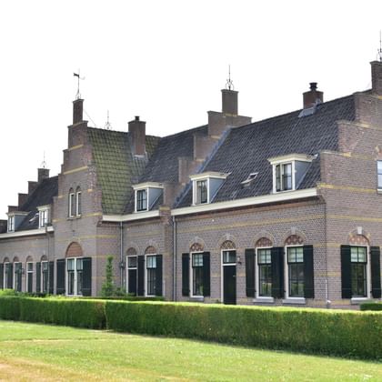 Historic Dutch brick house with green shutters Traditional Dutch brick house with green shutters, dormer windows, and multiple chimneys, surrounded by manicured hedges and lawn.