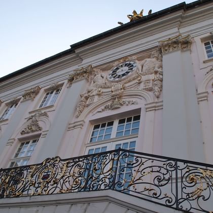Barocke Fassade des Bonner Rathauses mit ornamentalem weißen Stuck, zentraler Uhr, hohen Fenstern und elegantem schmiedeeisernen Balkon.