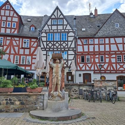 Traditional half-timbered buildings with red and white facades in Limburg's old town square, featuring a stone fountain and bicycles parked nearby.
