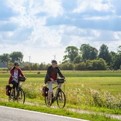 Cyclists on North Frisia cycle path Two cyclists with touring bikes and panniers on a rural road in North Frisia. Green fields, trees and wind turbines visible in background.