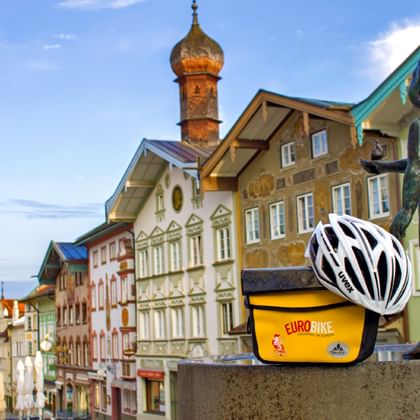Bad Tölz Stadtzentrum mit Fahrradhelm Blick auf Bad Tölz Zentrum mit bunten Barockgebäuden, Kirchturm mit Zwiebelkuppel und weißem Fahrradhelm auf Bronzestatue.