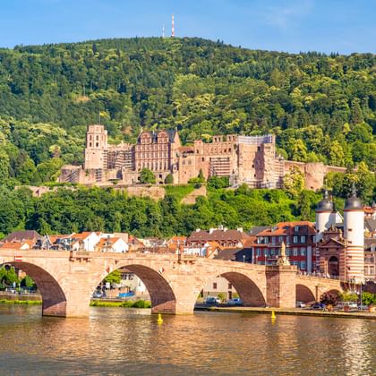 Heidelberger Alte Brücke über den Neckar mit der historischen Schlossruine am Hang über der Altstadt unter blauem Himmel.