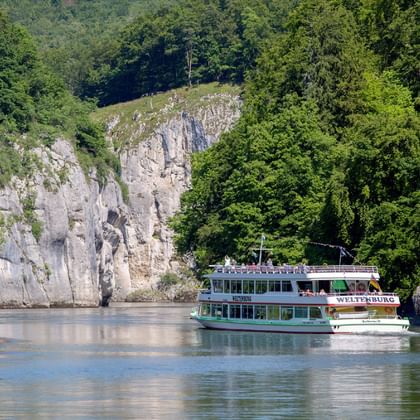 Touristenboot fährt durch den Donaudurchbruch am Kloster Weltenburg, umgeben von dramatischen Kalksteinfelsen und dichtem Wald.