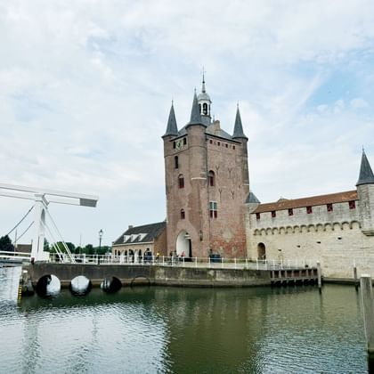 Medieval gate tower with pointed turrets in Zierikzee, Zeeland, connected by a white drawbridge over a canal. Boats moored on the left.