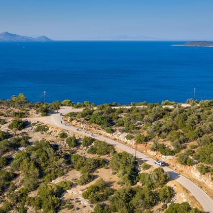 Peloponnese coastal landscape with winding road Aerial view of Peloponnese coastline with winding road through Mediterranean vegetation, overlooking blue sea with distant islands and mountains.