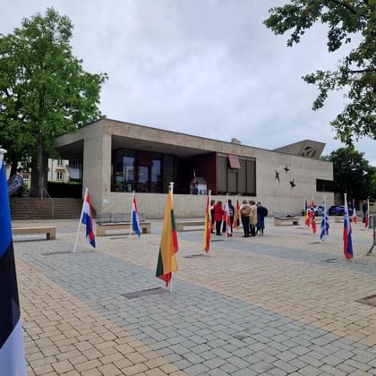 Modernes Betonmuseumsgebäude in Schengen mit gepflastertem Platz, auf dem mehrere europäische Nationalflaggen zu sehen sind.