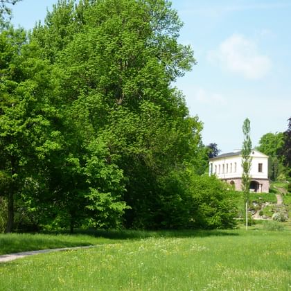 Park an der Ilm in Weimar with green meadow Green meadow with walking path in Park an der Ilm, Weimar. Large trees frame a white classical building in the background under blue sky.