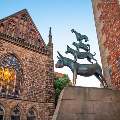 Bremen Town Musicians statue in Bremen Bronze statue of Bremen Town Musicians showing stacked animals - donkey, dog, cat and rooster - in front of historic brick church.