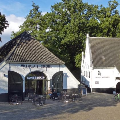Weiße historische Gebäude am Molenplaats Sonsbeek in Arnheim mit Außenterrasse und geparkten Fahrrädern, umgeben von grünen Bäumen.