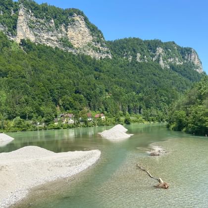 Türkisfarbener alpiner Stausee mit weißen Sedimentablagerungen und Treibholz. Dramatische Kalksteinfelsen erheben sich über dichtem Wald.