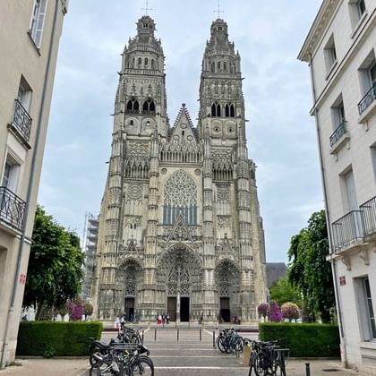 Gothic cathedral with twin spires and ornate facade viewed from street with parked bicycles and white residential buildings on both sides.