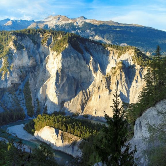 Dramatischer Blick auf die Rheinschlucht in der Schweiz mit weißen Kalksteinfelsen, dichtem Wald und gewundenem Fluss mit Bergen im Hintergrund.