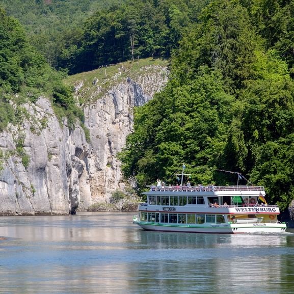 Touristenboot fährt durch den Donaudurchbruch am Kloster Weltenburg, umgeben von dramatischen Kalksteinfelsen und dichtem Wald.