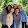 Five smiling team members standing together outdoors in a lush green park with trees in the background.